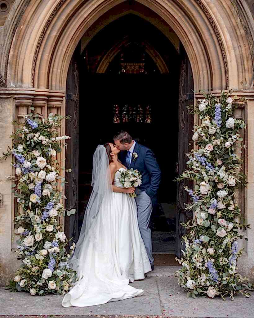 Bride at groom under arch outside of the church inside of broken arch of flowers
