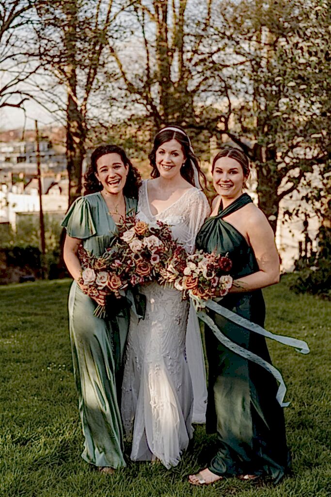 Bridesmaids in green dresses with bride holding autumnal florals