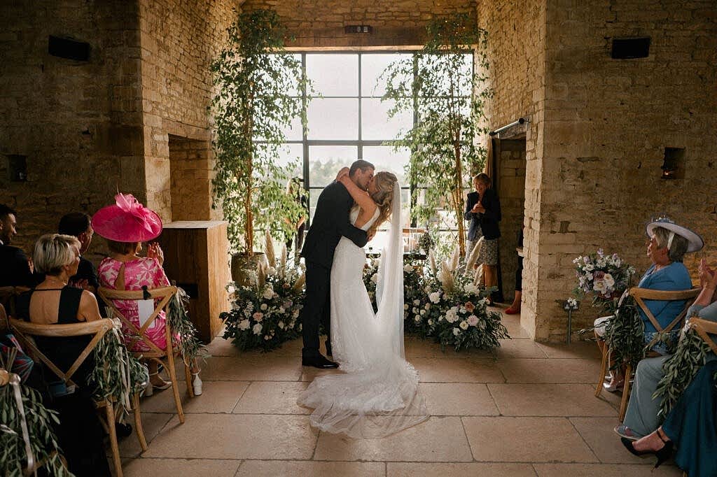 Bride and groom celebrating their marriage with a kiss in front of their florals