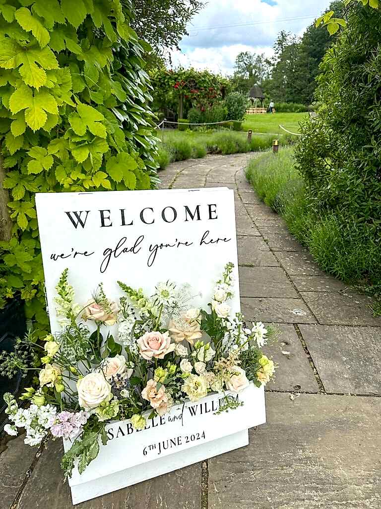 A board welcome sign for a wedding filled with netural florals